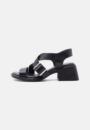 Black leather open-toe sandal with two straps, large silver buckle, and a mid-height chunky heel against a plain background.