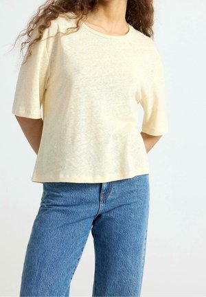 Crèmekleurig, kort mouwtjes, zacht katoenen t-shirt met een losse pasvorm en een ronde halslijn, gecombineerd met een hooggesloten blauwe spijkerbroek.