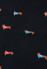 Námořnická pletenina s opakujícím se vzorem jezevčíků v červených a modrých svetrech, se vzory bílých sněhových vloček.