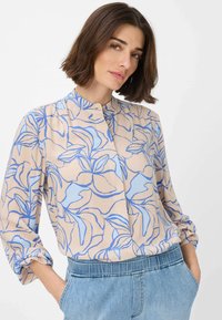 Camicia beige chiaro con motivo floreale blu; presenta un colletto alla mandarina, maniche lunghe e una vestibilità rilassata. Tessuto morbido e leggero.