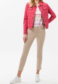 Chaqueta de mezclilla roja con bolsillos frontales, camisa blanca con rayas de colores, pantalones beiges ajustados y zapatillas blancas.