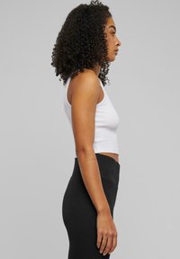 Witte cropped tanktop met dunne bandjes, gecombineerd met hoog getailleerde zwarte leggings. Soepele textuur, aangesloten ontwerp en minimalistische stijl.