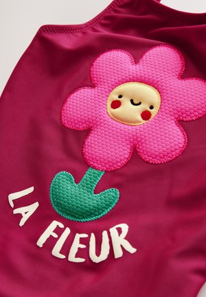 Costume da bagno fucsia con un design floreale rosa testurizzato che presenta un volto sorridente e uno stelo verde, accompagnato dal testo "LA FLEUR."