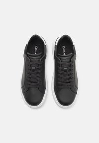 Baskets en cuir noir avec semelles blanches, dotées d'un design à lacets et d'un marquage discret sur la languette, texture lisse et bout arrondi.