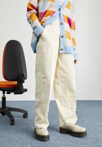 Pantalon blanc à jambes larges avec poches avant, associé à un cardigan surdimensionné multicolore et des chaussures à plateforme beige épaisses.