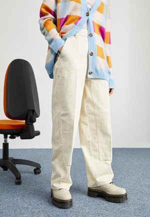 White, wide-leg trousers with front pockets, paired with a multicolored oversized cardigan and chunky beige platform shoes.