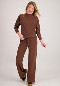 Bruin gebreide outfit met een trui met hoge hals en wijde broekspijpen, beide met een losse pasvorm en een trekkoorddetail. Geaccentueerd met bruine schoenen.