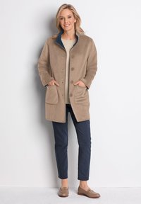 Beige Wolle-Mix-Mantel mit einem marineblauen Kragen, ausgestattet mit zwei Vordertaschen, Druckknopfverschluss und einer lässigen Passform. Kombiniert mit marineblauen Hosen.