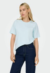 Lyseblå bomulds-T-shirt med rund halsudskæring og korte ærmer, parret med mørk denim jeans med kontrastsyninger.