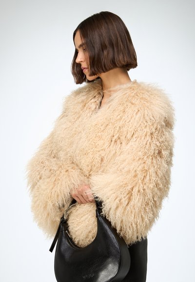 Fluffy beige faux fur jacket with voluminous sleeves, worn over a black leather dress, holding a curved black leather handbag.