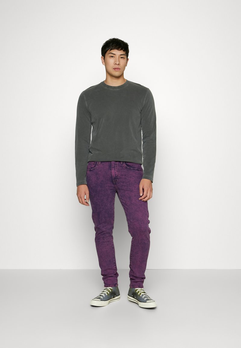 Camisa gris de manga larga, jeans skinny morados y zapatillas grises con suelas blancas. Ajuste casual, textura suave y color vibrante.