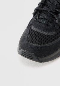 Detaljni prikaz vrha crne sportske tenisice s mrežastom tkaninom, preklopima od brušene kože i malim Jumpman logotipom na vezicama.