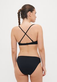 Black bikini set featuring a cross-back design, adjustable straps, and a clasp closure. Smooth texture and minimalistic style.