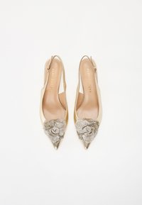 Tacones slingback beige con punteras puntiagudas, adornados con un embellecimiento floral de joyas. Acabado en cuero suave con acentos metálicos.