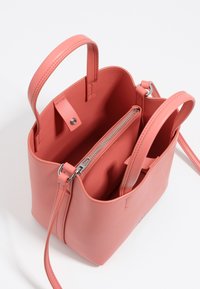 Bolso de piel rosa con dos asas y una correa de hombro desmontable, que cuenta con un compartimento interior con cremallera y una textura suave.