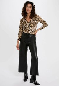 Suéter de estampado de leopardo con escote en V y bordes negros, combinado con pantalones de cuero sintético de cintura alta y perneras amplias en negro y botas de tobillo negras.