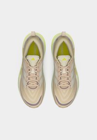 Ζευγάρι μπεζ και κίτρινα παπούτσια τρεξίματος Adidas, φωτογραφημένα από πάνω σε λευκό φόντο.