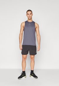 Grå ærmeløs atletisk T-shirt med rund hals; sorte shorts; sorte og grønne sneakers. Stoffet ser glat og letvægts ud.