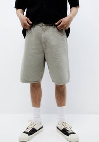 Shorts di cotone grigio chiaro con vestibilità rilassata, dotati di tasche frontali e orli cuciti. Abbinati a sneakers nere e crema e calze bianche.