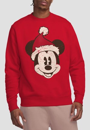 Mann trägt ein rotes Sweatshirt, auf dem vorne das Vintage-Style Gesicht von Mickey Mouse mit einer Weihnachtsmütze abgedruckt ist.