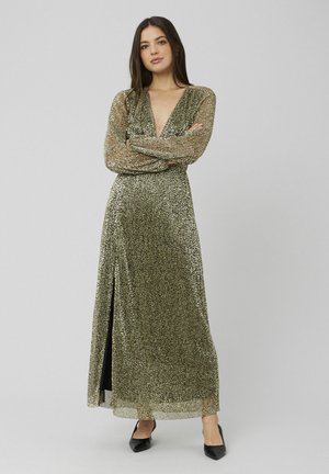 Longue robe dorée pailletée avec un décolleté plongeant, des manches longues et une fente latérale ; associée à des talons noirs. Texture lisse et détails scintillants.