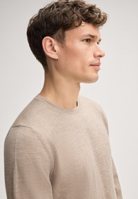 Beige Rundhals-Pullover aus weichem Strickstoff, mit langen Ärmeln und glatter Textur, entworfen für eine figurbetonte Silhouette.