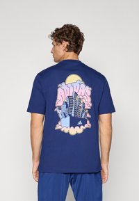 Mørkeblå bomulds T-shirt med et stort farverigt grafik af bygninger og skyer på ryggen, med en rund gul solaccent.