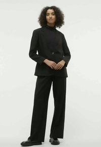 Czarny, dopasowany garnitur z marynarką na jeden guzik, szerokimi spodniami i dopasowanym czarnym golfem. Gładki materiał, minimalistyczny design, bez wzorów.