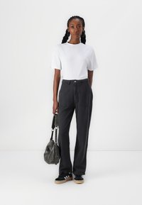 T-shirt blanc, coupe décontractée ; pantalon large et foncé avec poches avant ; baskets noires avec rayures blanches ; sac gris avec une bandoulière.