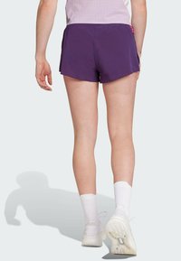 Ljubičaste sportske kratke hlače s zakrivljenim rubom i bočnim prorezima, izrađene od lagane tkanine. Nosene s bijelim čarapama i tenisicama.