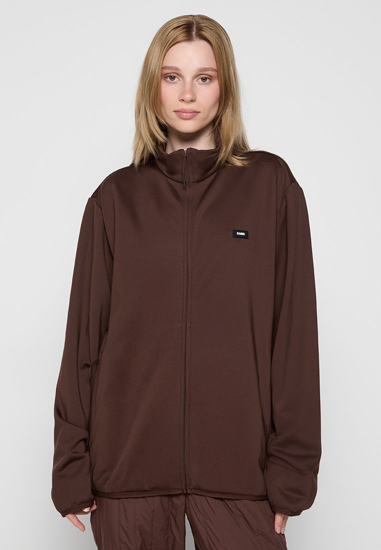 Braune Zip-Jacke aus einem glatten Material mit hohem Kragen und einem kleinen Logo-Patch auf der linken Brust. Locker sitzendes Design.