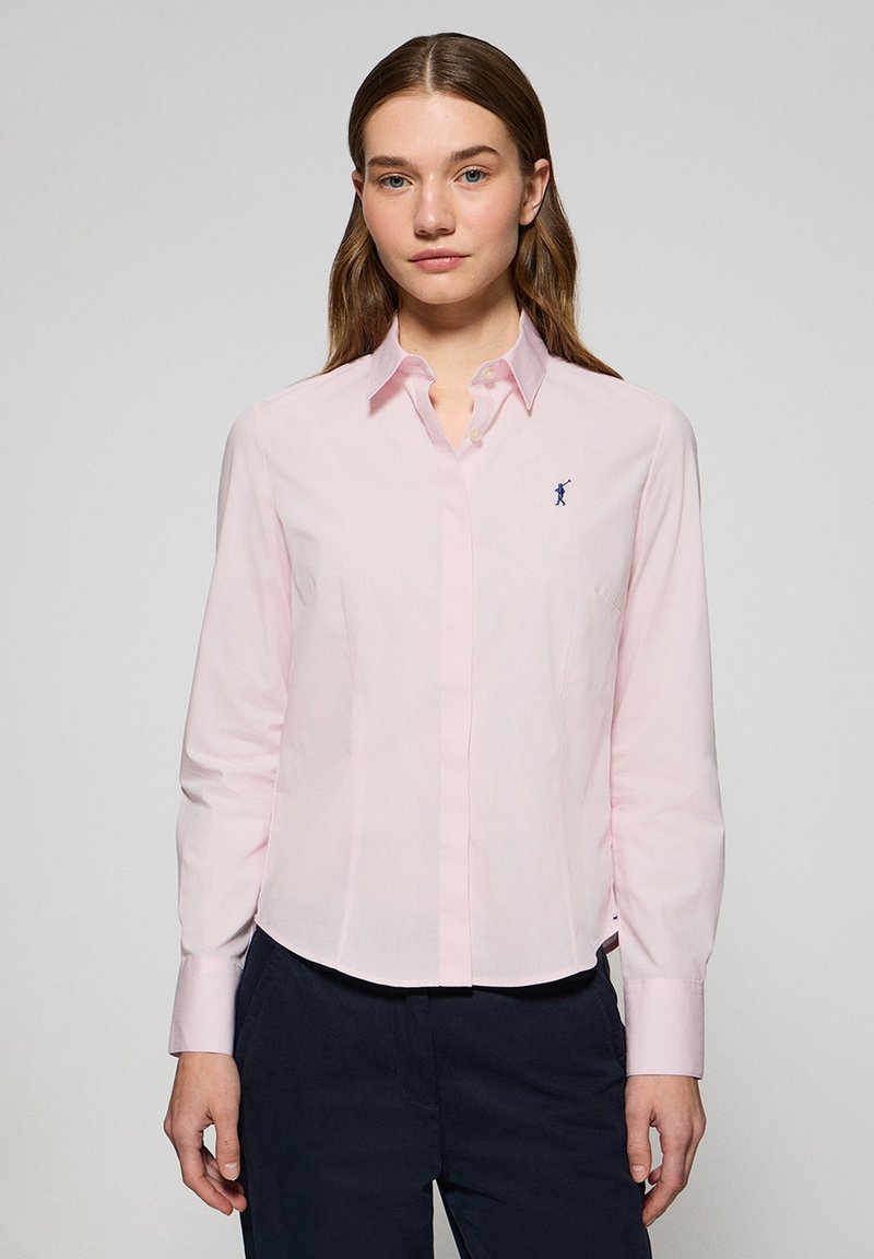 Jasnoróżowa koszula z długim rękawem, z kołnierzykiem w kształcie ostrego kąta oraz małym granatowym logo na piersi. Wykonana z bawełny o gładkiej fakturze.