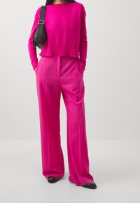 Helles pinkes, kurzes Sweatshirt mit geripptem Saum, kombiniert mit hellen pinken, weiten Hosen. Eine schwarze Schultertasche und schwarze Ballerinas runden das Outfit ab.