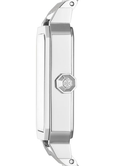 Côté du boîtier de montre-bracelet en métal argenté avec couronne octogonale présentant un logo gravé et des éléments de design anguleux polis.