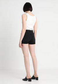 Mustat korkeavyötäröiset farkkushortsit, joissa on viiden taskun muotoilu. Yhdistetty valkoiseen hihattomaan toppiin ja mustiin korkokenkämuleihin.