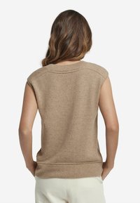 Stickad ärmlös tröja i ljusbeige med ribbad halsringning och fåll. Mjuk textur och subtila sömdetaljer över axlarna.