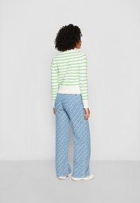 Häkelpullover in Weiß mit grünen Streifen; gemusterte blaue weit geschnittene Hosen; weiche Textur, lockere Passform, knöchellang, lässiger Stil.