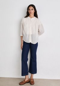 Camicia a bottoni di un crema chiaro, con texture a righe, colletto rotondo e maniche a tre quarti abbinata a jeans svasati blu scuro e mocassini marroni.