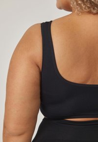Czarny top na ramiączkach z prążkowanej tkaniny, z szerokimi ramiączkami i niskim dekoltem z tyłu, z wycięciem poniżej pleców dla dodatkowego detalu.