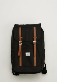 Black fabric backpack with brown leather straps and silver metal hardware. Features a flap closure and front pocket.
