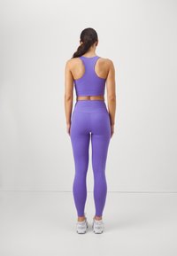 Μωβ αθλητική εμφάνιση που περιλαμβάνει ένα αθλητικό σουτιέν με πλάτη racerback και ψηλόμεσα κολάν, με απαλή, ελαστική ύφανση και σχέδιο που αγκαλιάζει το σώμα.