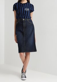 Niebieska koszulka w paski z logo, zestawiona z ciemną dżinsową spódnicą midi. Czarne sneakersy dopełniają stylizację w casualowym stylu.