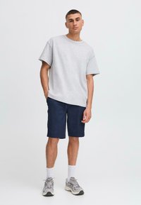 T-shirt gris à manches courtes, coupe décontractée, associé à un short bleu marine. Le modèle porte des chaussettes blanches et des baskets grises. Design minimaliste, sans logos visibles.