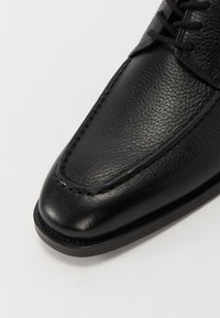 Scarpa in pelle nera con finitura texturizzata, caratterizzata da una punta arrotondata e dettagli cuciti lungo il bordo. Accenti lisci e opachi.
