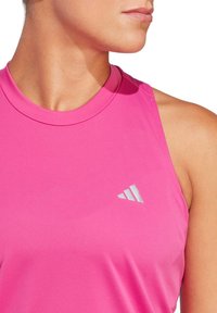 Top deportivo rosa de tirantes, hecho de una tela suave y elástica; presenta un escote redondo y un pequeño logo plateado en el lado izquierdo.
