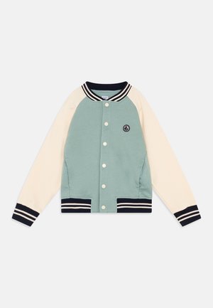 Veste varsity boutonnée avec corps vert clair, manches crème, poignets, col et bas rayés bleu marine, et un petit logo circulaire sur la poitrine.