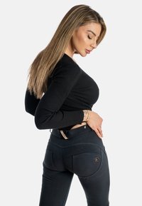 Musta ribattu pitkähihais-toppi yhdistettynä tummaan, slim fit -farkkuihin, joissa on takataskut ja logoaksentti vyötärön lähellä.