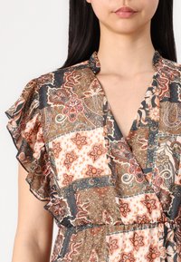 Daudzkrāsains kleita ar artavu dizainu, kurā ir ziedu un paisley raksti. Rūtainas piedurknes un V veida kakla izgriezums pievieno tekstūru.