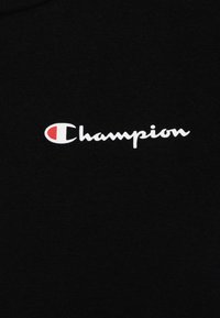T-shirt en coton noir avec le texte "Champion" en blanc et une accentuation rouge sur la lettre "C". Texture lisse, design décontracté, col rond.