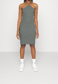 Szara dopasowana sukienka z dekoltem na halter, wykonana z elastycznego materiału. Noszona z białymi sneakersami i skarpetkami.